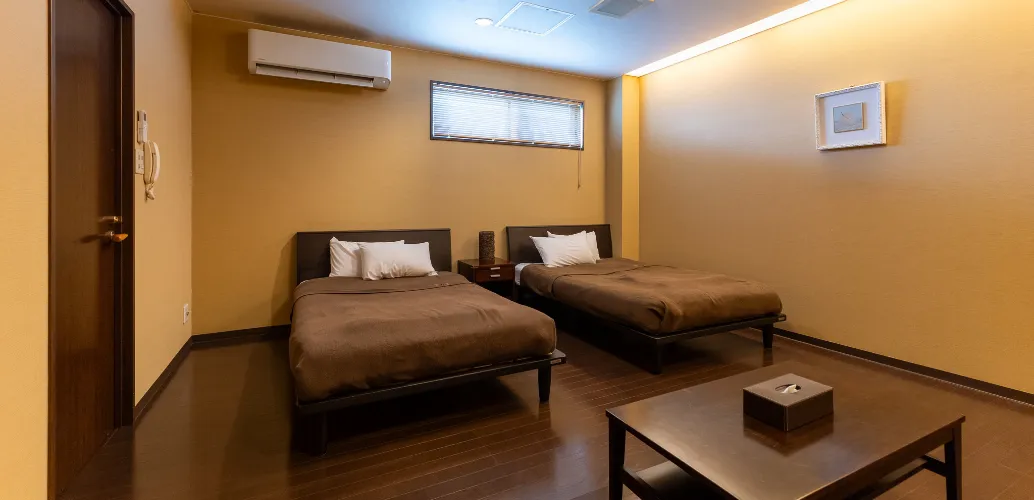 写真：エアコン、シングルベッドが2台、四角形のテーブルがあるベッドルーム